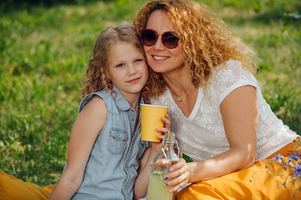 Portrait of a mother and daughter during a picnic on grass in the gardens - Photo, Image