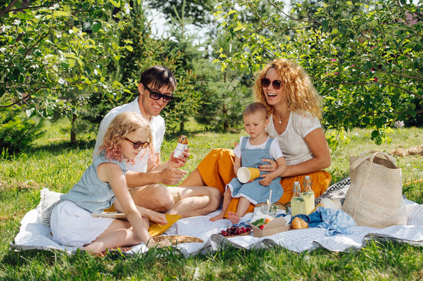 Piknik rodzinny na trawie w ogrodach pod delikatnym odcieniem drzew - Zdjęcie, obraz
