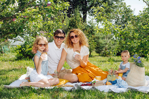 Familie picknick op gras in de tuinen onder zachte schaduw van bomen - Foto, afbeelding