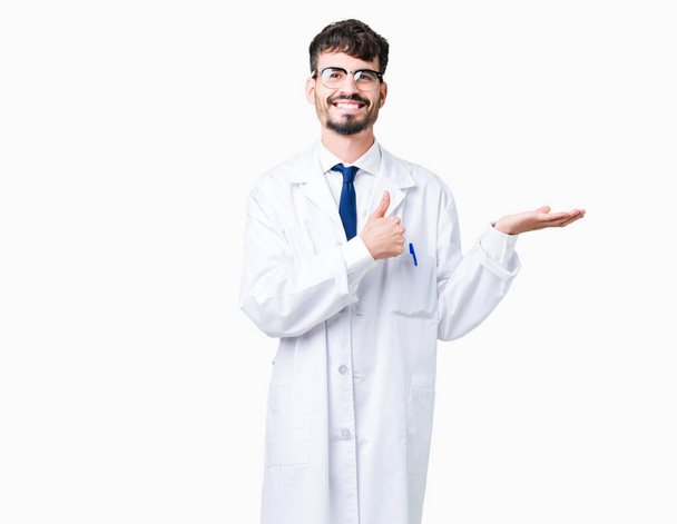 Young professional scientist man wearing white coat over isolated background Showing palm hand and doing ok gesture with thumbs up, smiling happy and cheerful - Fotó, kép
