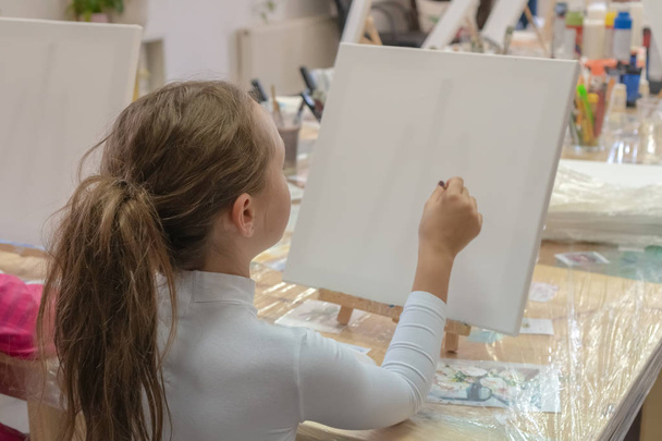 Красива дівчина з пензлем в руці. Творчий підліток практикує малювання в художній школі. Інтер'єр художньої школи для малювання дітей. Творчість і концепція людей
. - Фото, зображення