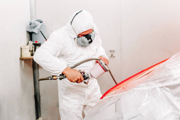 Portrait of auto manufacturing industry worker with spray gun with red paint painting a car in special booth - Фото, зображення