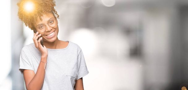 Genç Afro-Amerikan kadın smartphone üzerinde duran ve diş gösterilen kendine güvenen bir gülümsemeyle gülümseyerek mutlu bir yüz ile izole arka plan üzerinde söz - Fotoğraf, Görsel