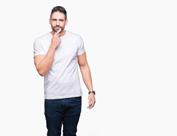Young man wearing casual white t-shirt over isolated background looking confident at the camera with smile with crossed arms and hand raised on chin. Thinking positive. - Fotografie, Obrázek