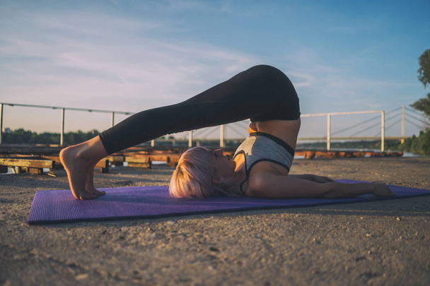 Frau praktiziert Yoga an sonnigen Tagen. Halasana / Pflug Pose - Foto, Bild