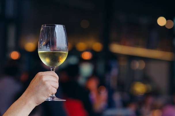 Hand hält ein Glas Weißwein mit buntem Bokeh-Licht. - Foto, Bild