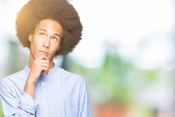 Afro-amerikai fiatalember afro haj kézzel a chin gondolkodás kérdés, töprengő kifejezés. Mosolygós, figyelmes arccal. Kétség koncepció. - Fotó, kép
