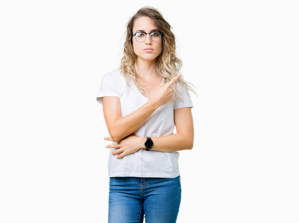 Beautiful young blonde woman wearing glasses over isolated background Pointing with hand finger to the side showing advertisement, serious and calm face - Foto, immagini
