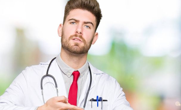 Jeune homme beau médecin vêtu d'un manteau médical pressé de regarder le temps, l'impatience, contrarié et en colère pour retard de délai
 - Photo, image