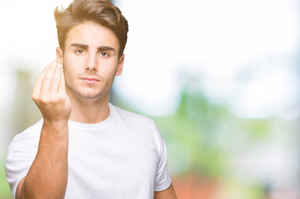junger gutaussehender Mann trägt weißes T-Shirt über isoliertem Hintergrund und macht italienische Geste mit selbstbewusstem Ausdruck an Händen und Fingern - Foto, Bild