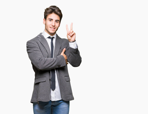 Young business man wearing suit and tie over isolated background smiling with happy face winking at the camera doing victory sign. Number two. - Photo, Image