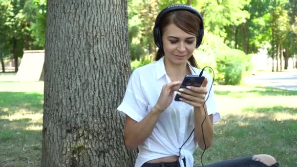Young girl listening to music on the phone in the Park - Кадры, видео