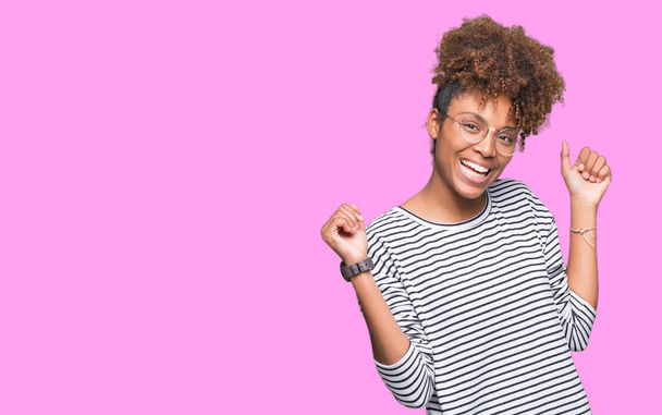 Красива молода афро-американських жінка в окулярах над ізольованих фону, танці, веселий і Бадьорий, посміхаючись рухомих випадковим і впевнено прослуховування музики - Фото, зображення