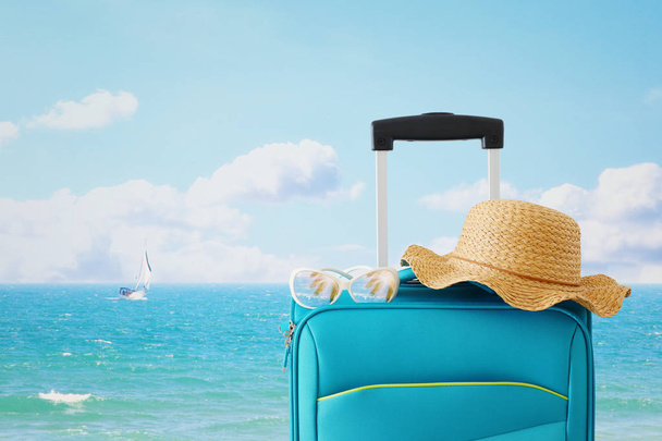 holidays. travel concept. blue suitcase with female hat, sunglasses in front of tropical background - Fotó, kép