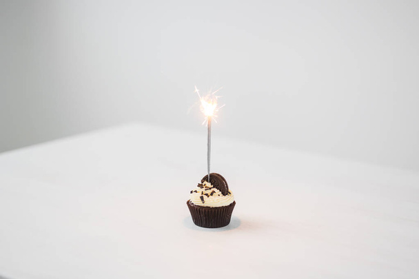 Conceito de comida, festa e feriado - Cupcake de aniversário com sparkler sobre fundo branco com espaço de cópia
 - Foto, Imagem