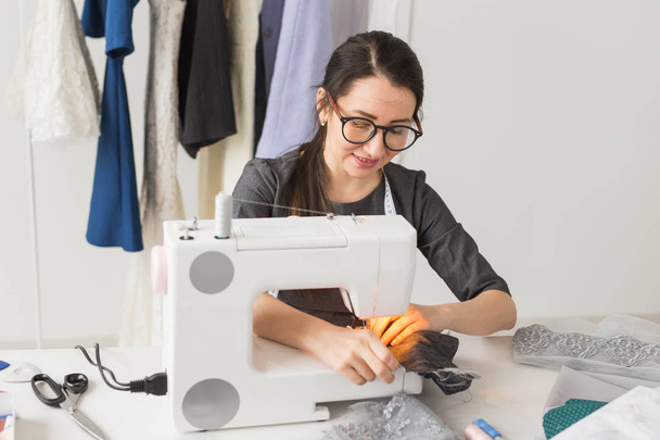 mensen, mode en showroom concept - jonge modeontwerper naait kleding op een naaimachine - Foto, afbeelding