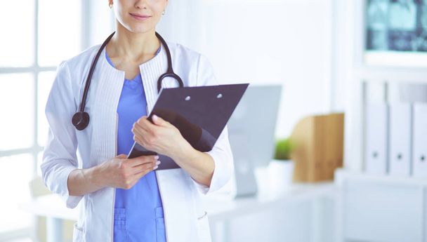 Young smiling female doctor with stethoscope holding a folder at doctors office - Photo, Image
