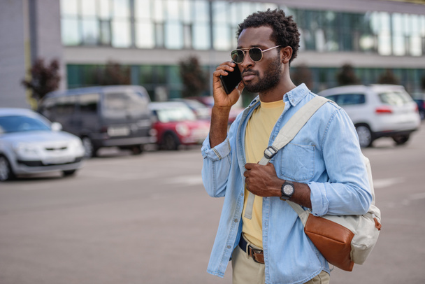 bello afro americano uomo parlando su smartphone mentre in piedi sul parcheggio auto e guardando altrove
 - Foto, immagini