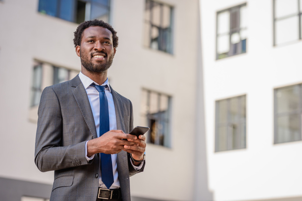 homme d'affaires afro-américain joyeux regardant loin tout en tenant smartphone
 - Photo, image