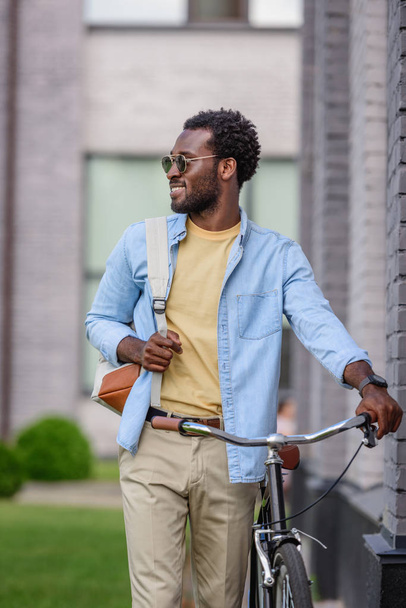 tyylikäs afrikkalainen amerikkalainen mies aurinkolaseissa katselee pois seistessään polkupyörän kanssa
 - Valokuva, kuva