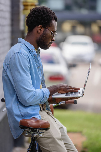 bel homme afro-américain utilisant un ordinateur portable tout en se tenant près du vélo
 - Photo, image
