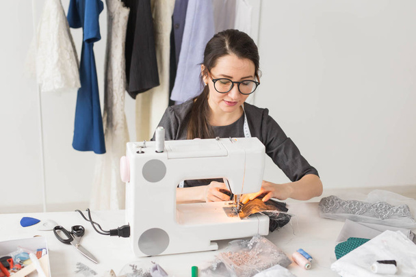 άνθρωποι, μόδα και showroom έννοια - Νεαρά σχεδιαστής μόδας ράβει ρούχα σε μια ραπτομηχανή - Φωτογραφία, εικόνα
