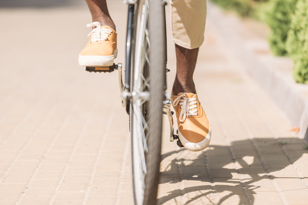 cropped view of african american man riding bicycle along sunny street - Photo, Image