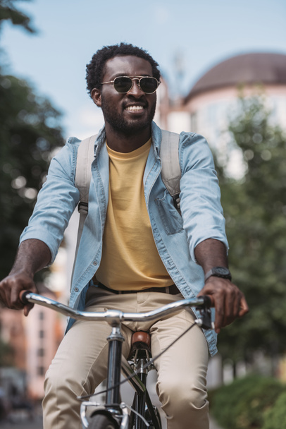 stijlvolle African American man op zoek weg en glimlachend tijdens het rijden fiets - Foto, afbeelding