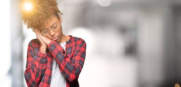 schöne junge afrikanisch-amerikanische Frau trägt eine Brille über isoliertem Hintergrund und schläft müde träumend und posiert mit den Händen zusammen, während sie mit geschlossenen Augen lächelt. - Foto, Bild