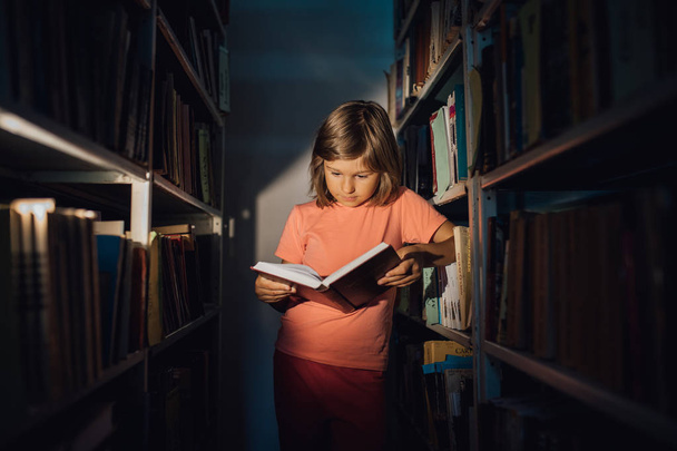 little girl learns in the library. holds a book in your hand, indoors, 1 - Фото, изображение