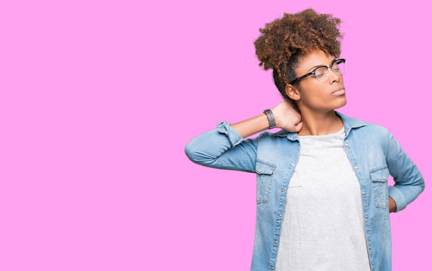 schöne junge afrikanisch-amerikanische Frau trägt eine Brille über isoliertem Hintergrund und leidet unter Nackenschmerzen, Berührung des Nackens mit der Hand, Muskelschmerzen - Foto, Bild