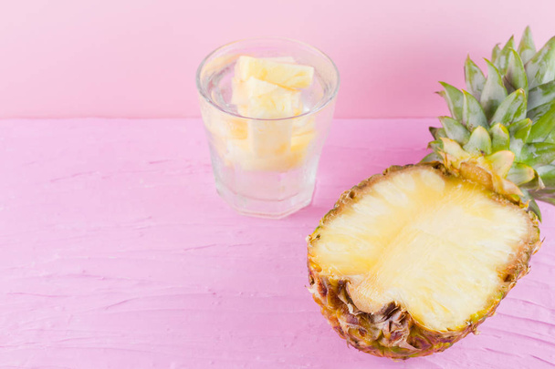Pineapple and infused water on a pink background. Half of pineapple on a pastel background. Cocktail with pineapple and ice. Minimalism. Copy space - Fotó, kép