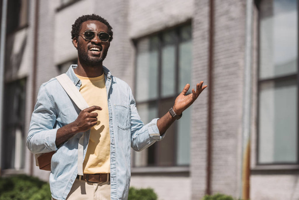 cheerful african american man in sunglasses smiling and gesturing while looking at camera - Fotoğraf, Görsel