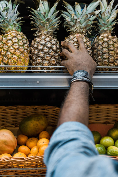 cropped view of african american man touching pineapple in supermarket  - Foto, afbeelding