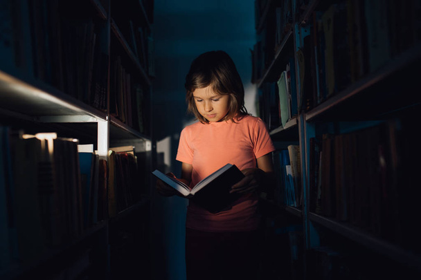 little girl reads the book, learns in the library, indoors, 1 - Фото, изображение