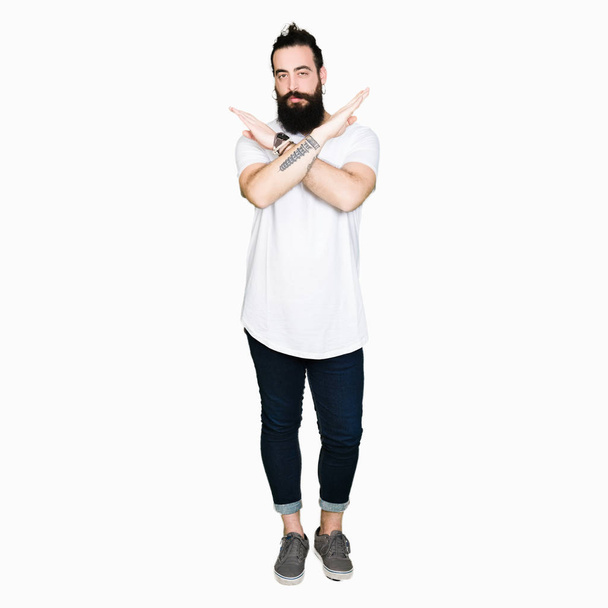 Jeune homme hipster aux cheveux longs et à la barbe portant un t-shirt blanc décontracté expression de rejet croisant les bras faisant signe négatif, visage en colère
 - Photo, image