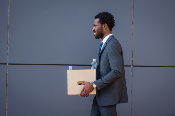 side view of handsome african american businessman holding cardboard box - Photo, Image