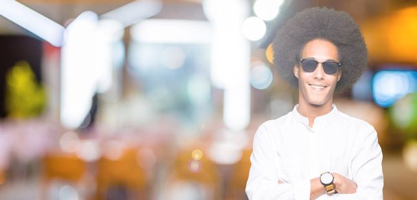 Молодий афроамериканець людиною з афро волосся носити сонцезахисні окуляри щасливим обличчям посміхається з схрещеними руками, дивлячись на камеру. Позитивна людина. - Фото, зображення