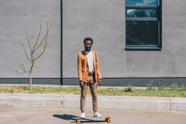 handsome african american businessman riding longboard on sunny street - Photo, Image