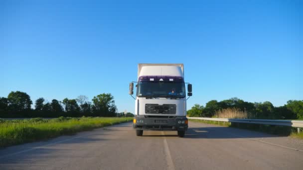 Yaz günü mal taşıma karayolu üzerinde sürüş kargo römork ile kamyon ön görünümü. Beyaz kamyon arka planda güzel manzara ile kırsal üzerinden sürme. Yavaş mo Ön görünüm Kapat - Video, Çekim