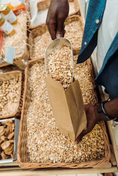abgeschnittene Ansicht eines afrikanisch-amerikanischen Mannes, der eine Metallschaufel mit leckeren Erdnüssen im Laden hält  - Foto, Bild