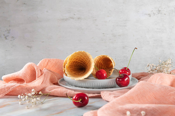 Traditional waffle cones and cherry fruits on marble stone surface. - Photo, Image