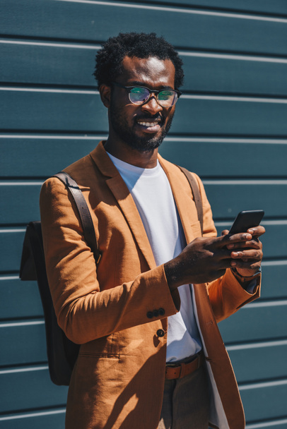 hombre de negocios afroamericano positivo mirando la cámara mientras usa el teléfono inteligente
 - Foto, Imagen