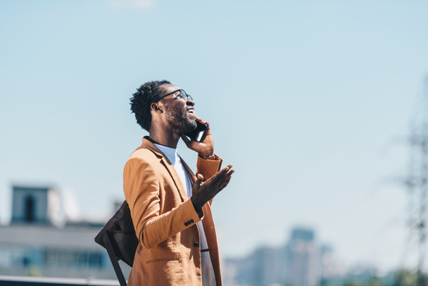homme d'affaires afro-américain souriant parlant sur smartphone et geste avec ciel bleu en arrière-plan
 - Photo, image