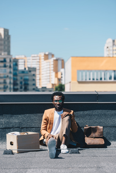 depressed african american businessman sitting on rooftop near carton box - Фото, зображення