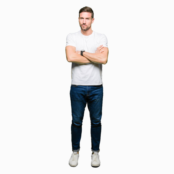 Handsome man wearing casual white t-shirt skeptic and nervous, disapproving expression on face with crossed arms. Negative person. - Photo, image