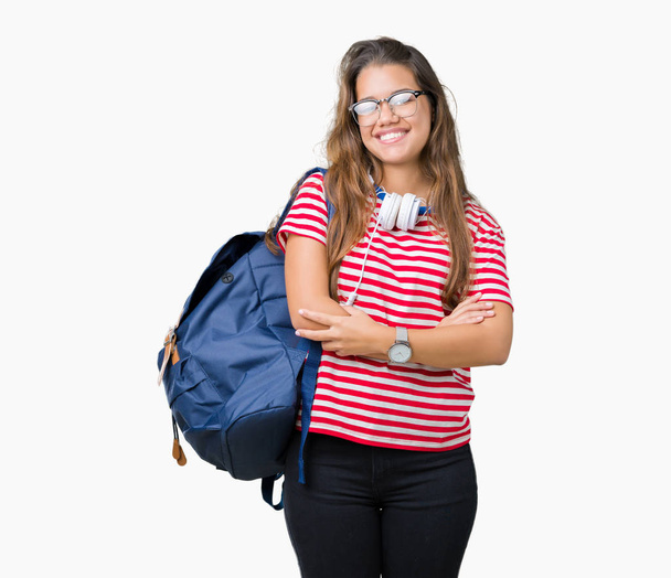 Young beautiful brunette student woman wearing headphones and backpack over isolated background happy face smiling with crossed arms looking at the camera. Positive person. - Foto, imagen