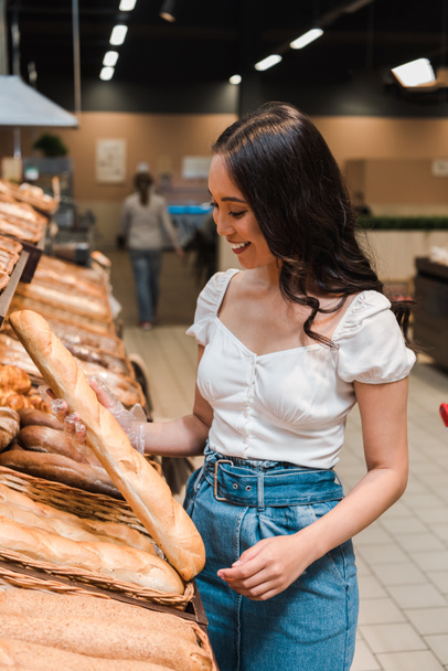 feliz asiático mujer sonriendo mientras celebración baguette en supermercado
  - Foto, imagen