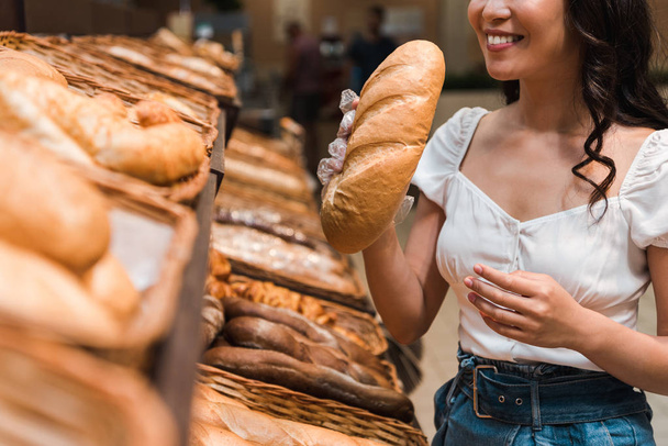 cropped view of happy woman smiling while smelling bread in supermarket  - Photo, image