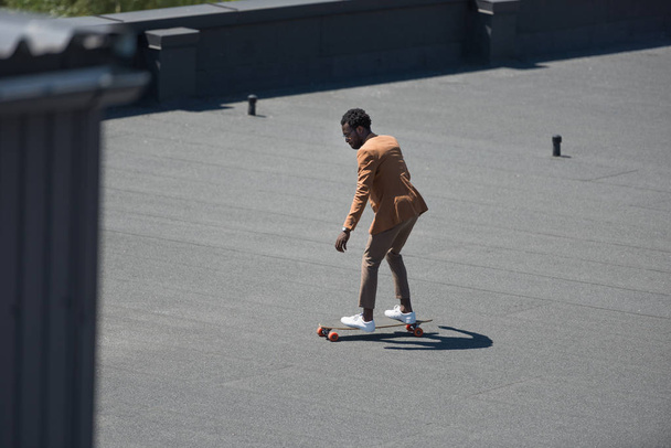 african american businessman riding longoard on sunny rooftop - Foto, afbeelding